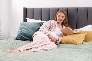 Photo of Beautiful pregnant woman reading book on bed at home