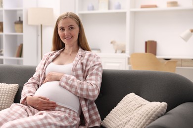 Photo of Beautiful pregnant woman on sofa at home. Space for text