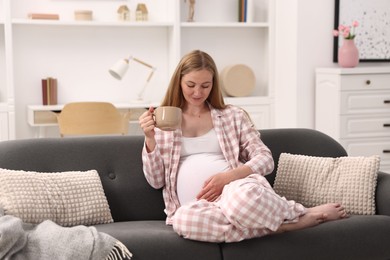 Photo of Beautiful pregnant woman with cup of drink on sofa at home