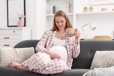 Photo of Beautiful pregnant woman with cup of drink on sofa at home