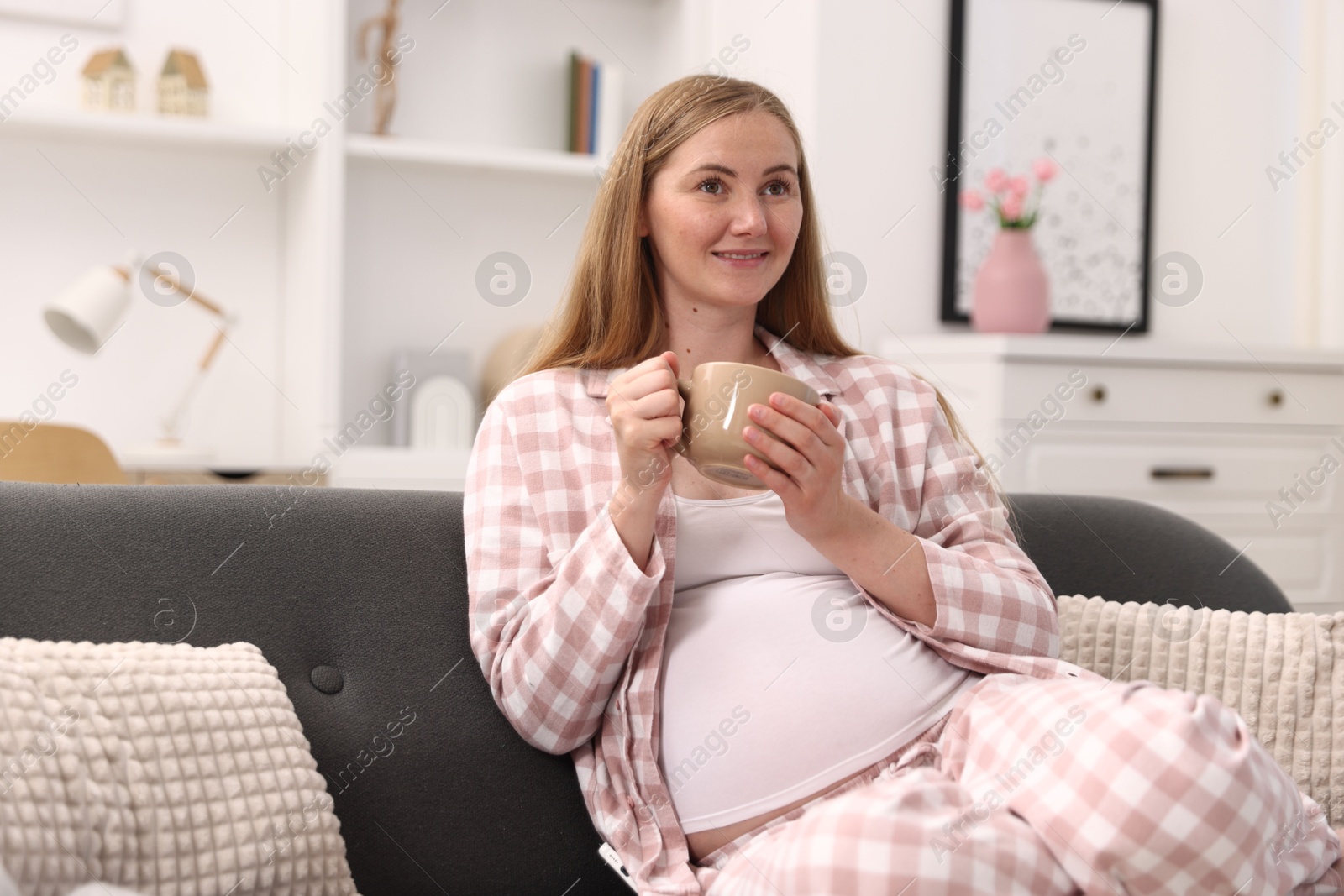 Photo of Beautiful pregnant woman with cup of drink on sofa at home