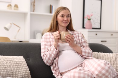 Photo of Beautiful pregnant woman with cup of drink on sofa at home