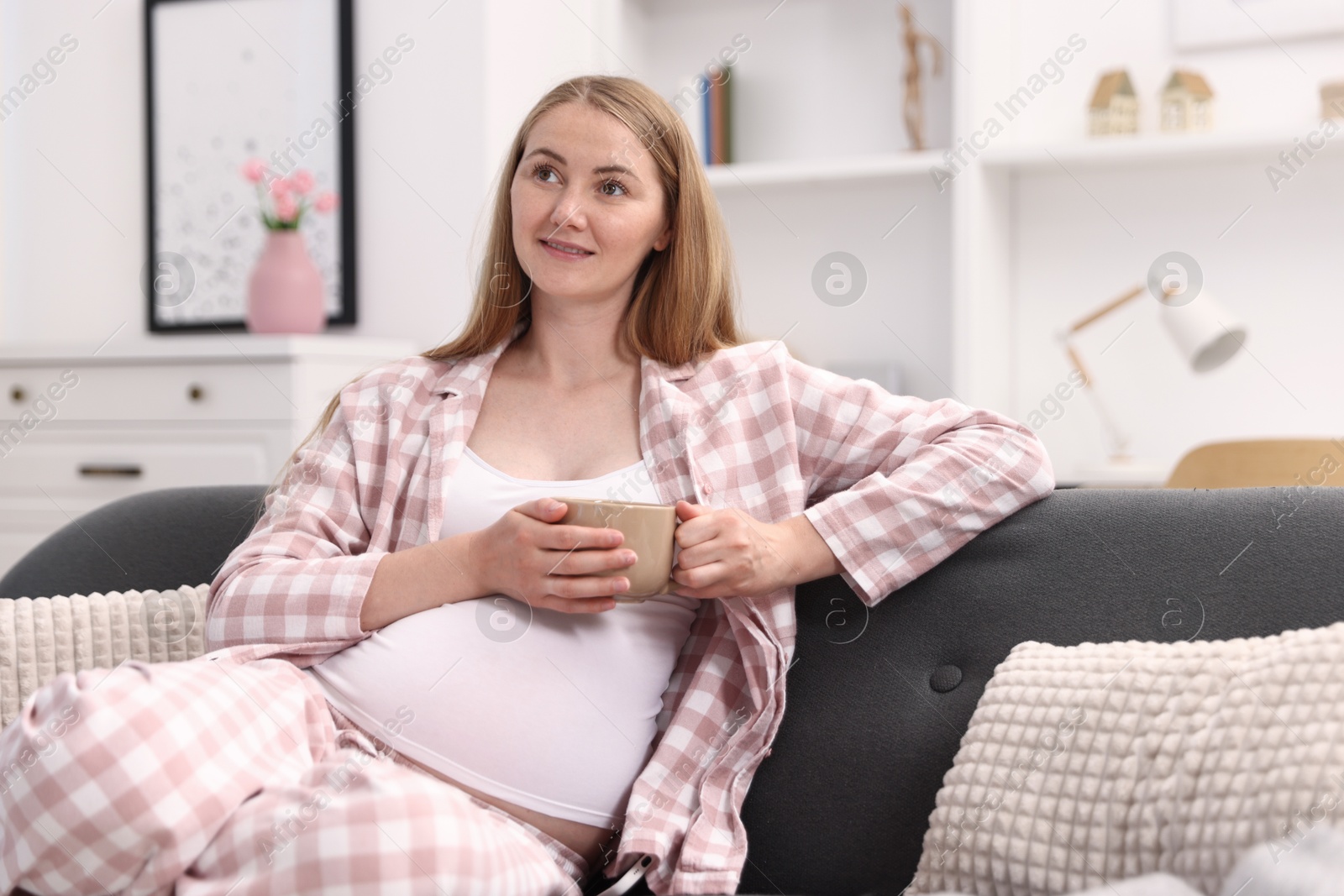 Photo of Beautiful pregnant woman with cup of drink on sofa at home