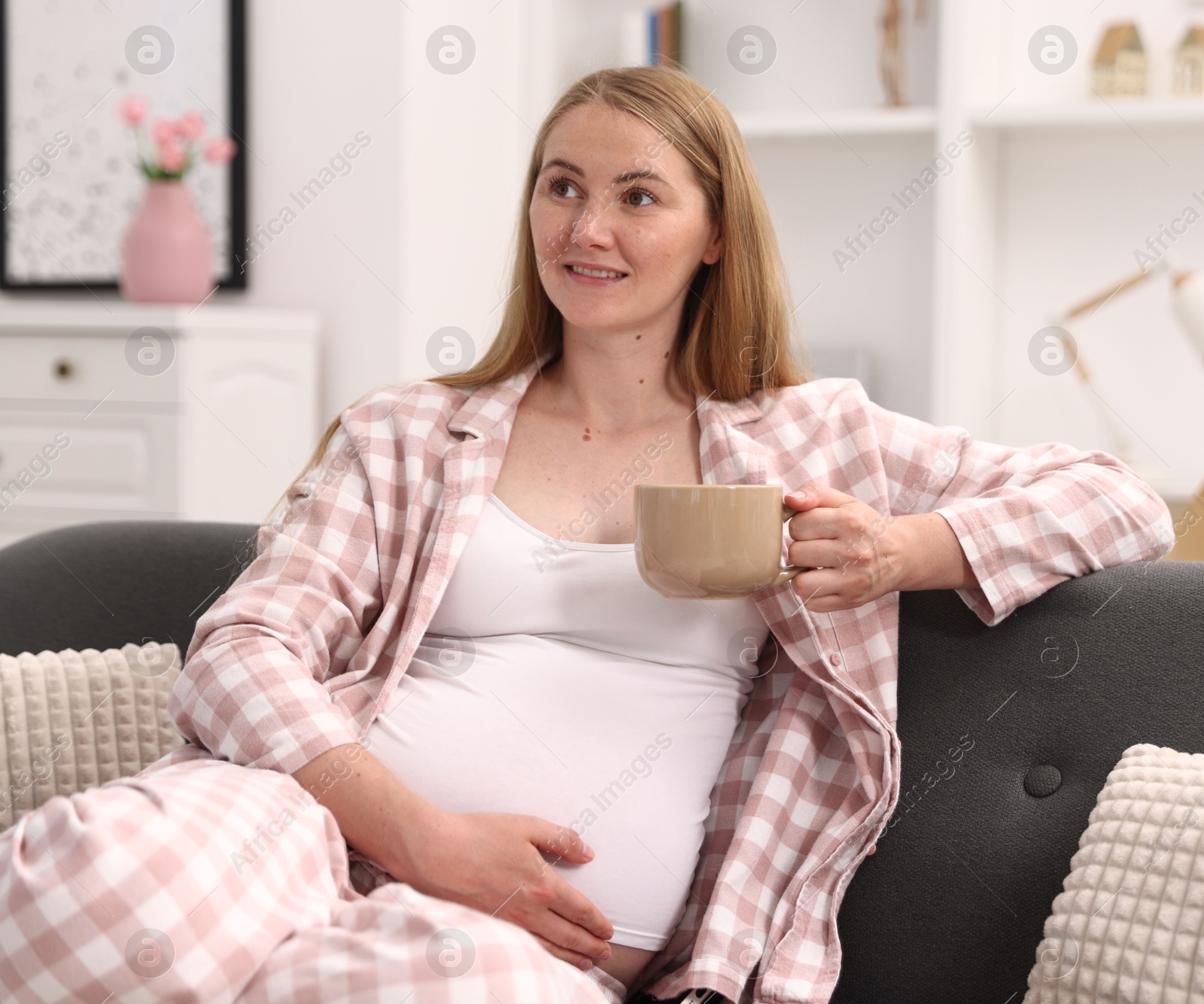 Beautiful pregnant woman with cup of drink on sofa at home Photo of Beautiful pregnant woman with cup of drink on sofa at home
