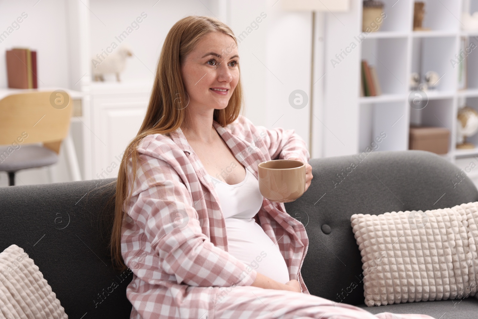 Beautiful pregnant woman with cup of drink on sofa at home Photo of Beautiful pregnant woman with cup of drink on sofa at home