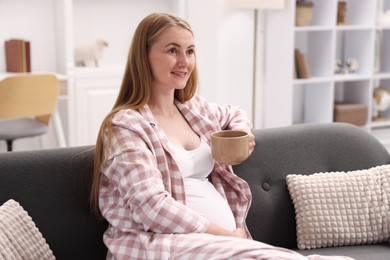 Photo of Beautiful pregnant woman with cup of drink on sofa at home