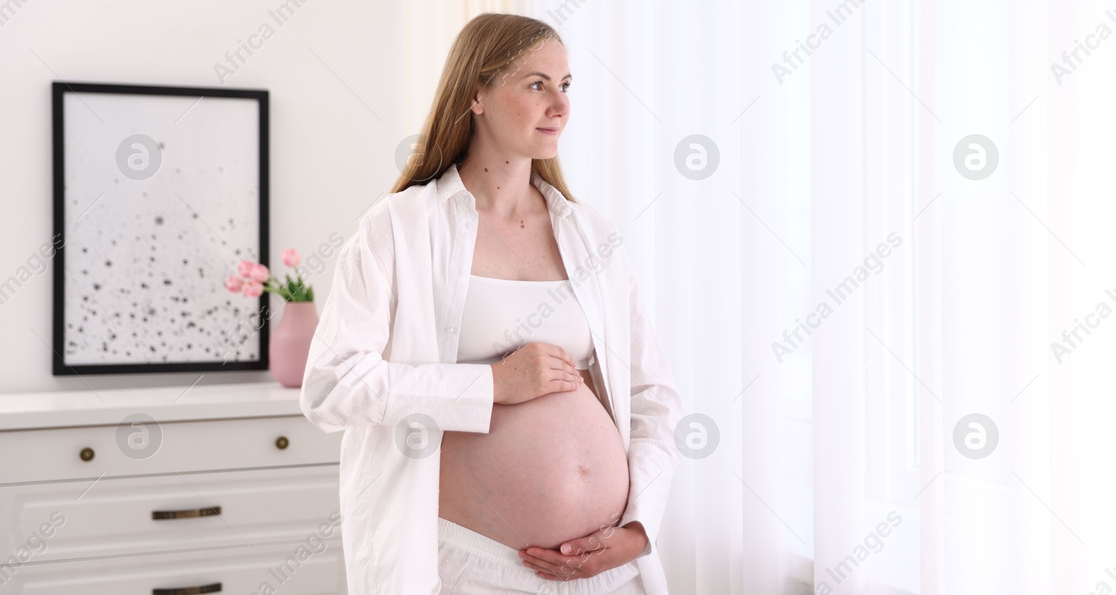 Photo of Beautiful pregnant woman touching her belly at home. Space for text