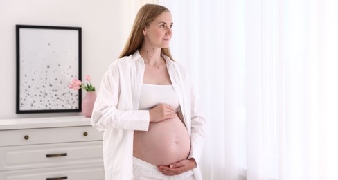 Photo of Beautiful pregnant woman touching her belly at home. Space for text
