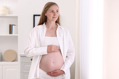 Photo of Beautiful pregnant woman touching her belly at home. Space for text