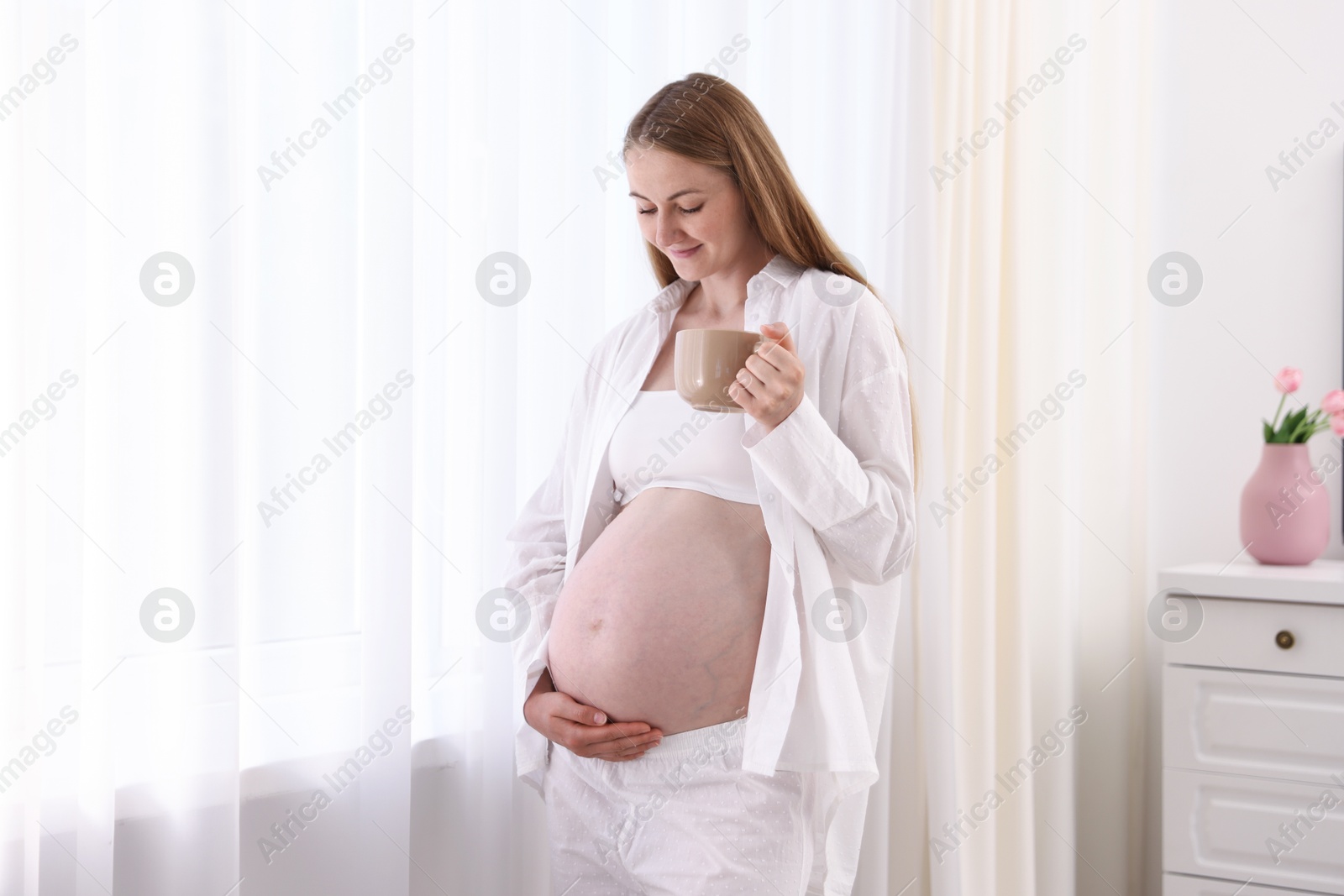 Beautiful pregnant woman with cup of drink at home Photo of Beautiful pregnant woman with cup of drink at home