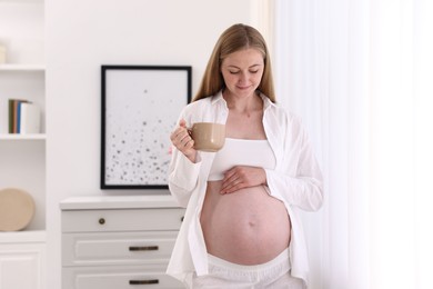 Photo of Beautiful pregnant woman with cup of drink at home