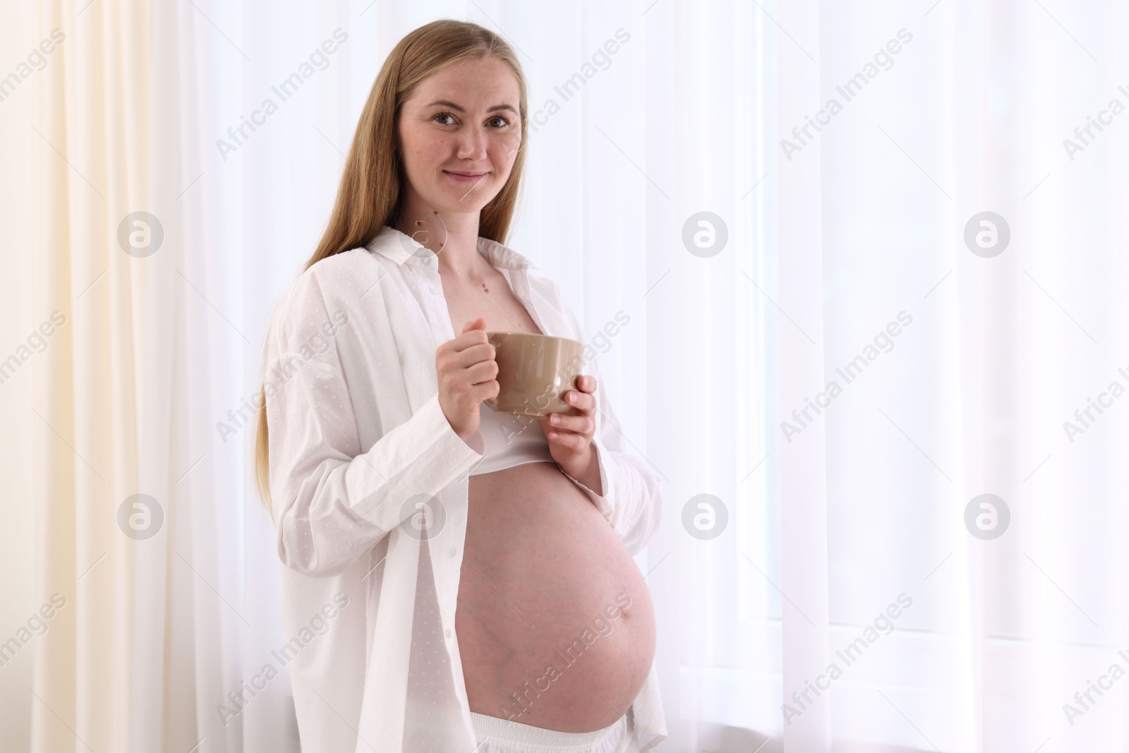 Photo of Beautiful pregnant woman with cup of drink at home. Space for text