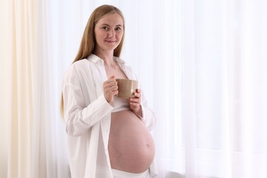 Photo of Beautiful pregnant woman with cup of drink at home. Space for text