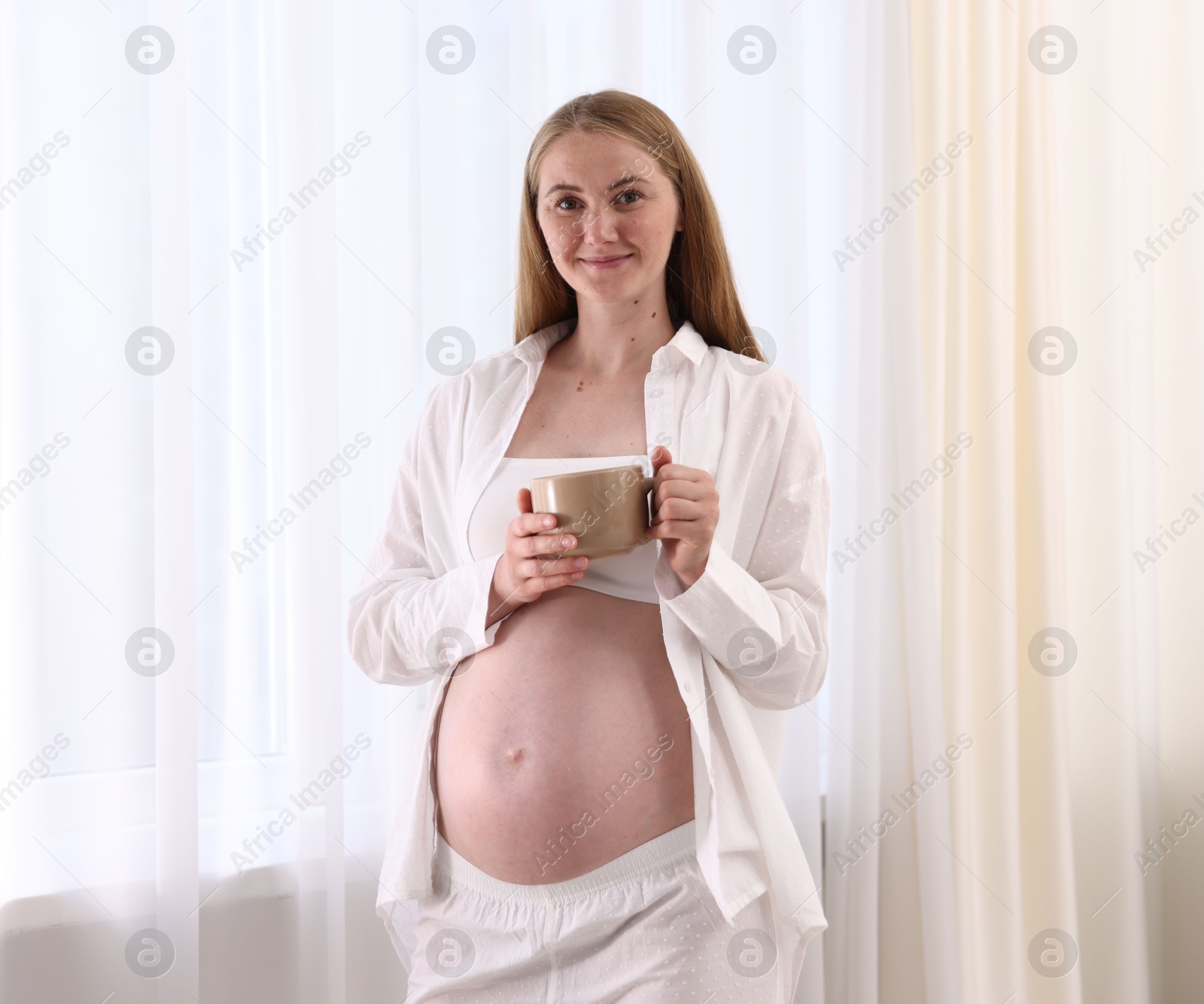 Beautiful pregnant woman with cup of drink at home Photo of Beautiful pregnant woman with cup of drink at home