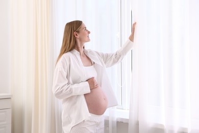 Photo of Beautiful pregnant woman near window at home