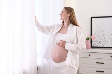Photo of Beautiful pregnant woman near window at home