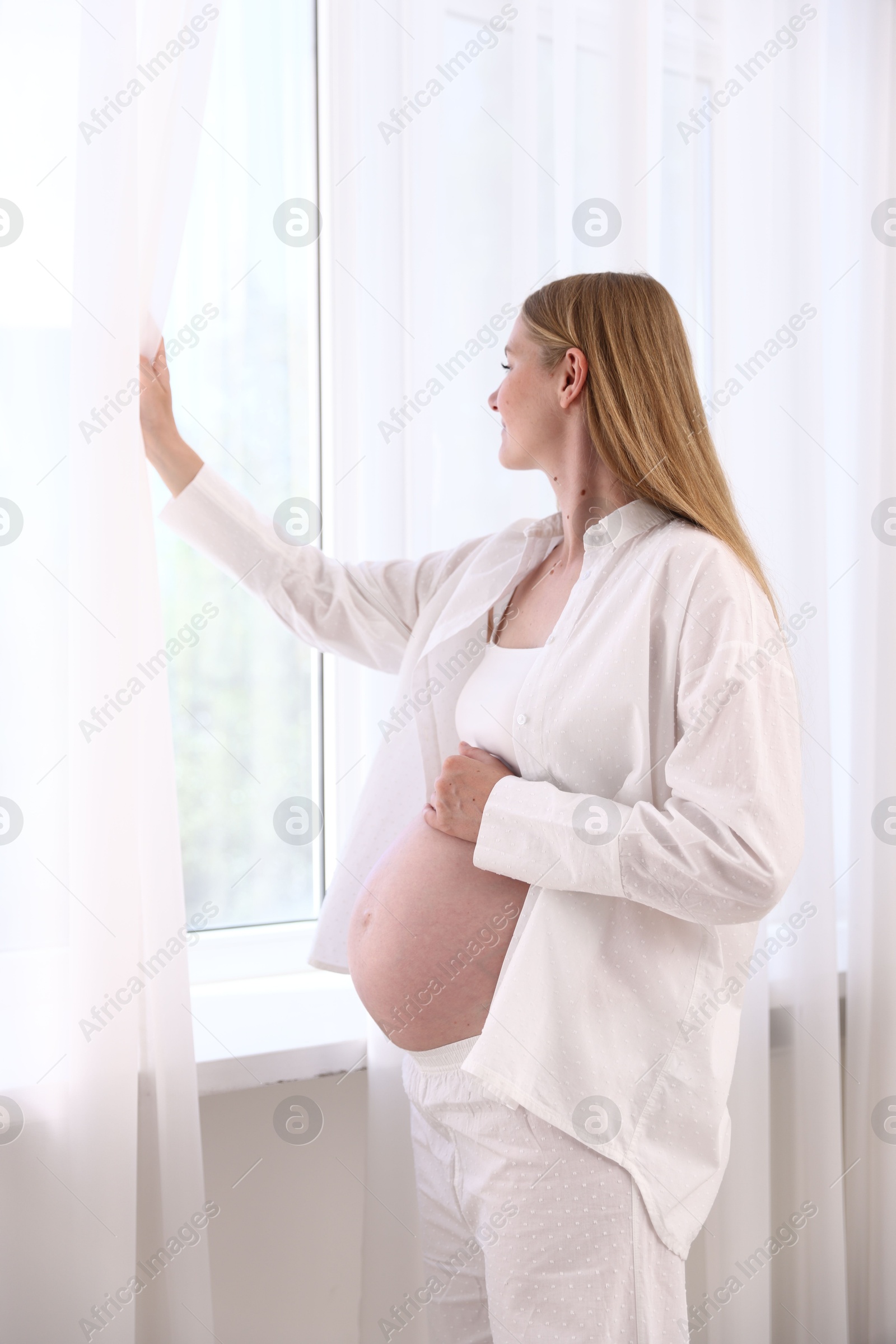 Photo of Beautiful pregnant woman near window at home