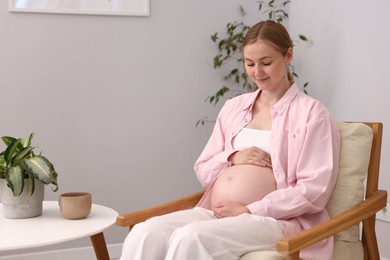 Photo of Beautiful pregnant woman in armchair at home. Space for text