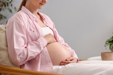 Photo of Beautiful pregnant woman in armchair at home, closeup. Space for text