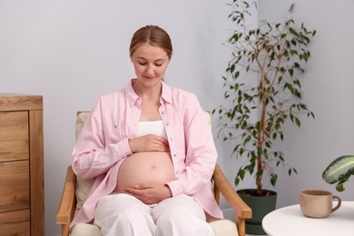 Photo of Beautiful pregnant woman in armchair at home