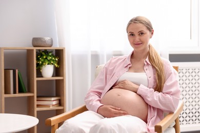 Photo of Beautiful pregnant woman in armchair at home. Space for text