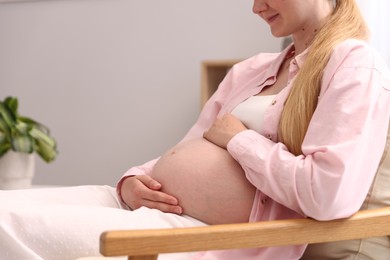 Photo of Beautiful pregnant woman in armchair at home, closeup. Space for text
