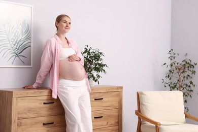 Photo of Beautiful pregnant woman touching her belly at home. Space for text