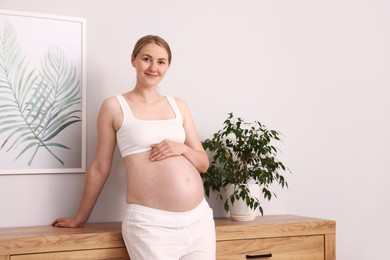 Photo of Beautiful pregnant woman touching her belly at home. Space for text