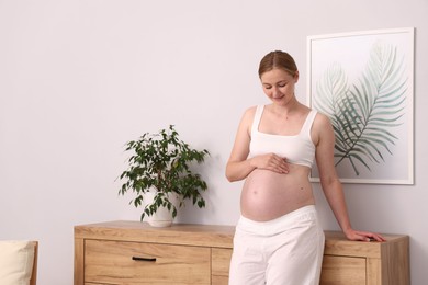 Photo of Beautiful pregnant woman touching her belly at home. Space for text