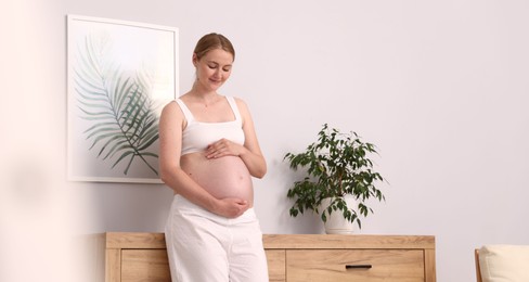 Photo of Beautiful pregnant woman touching her belly at home. Space for text