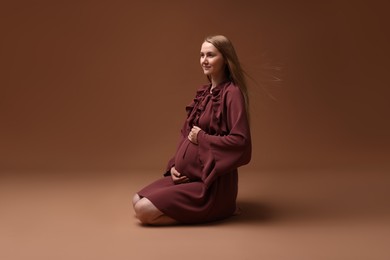 Photo of Beautiful pregnant woman in dress on brown background