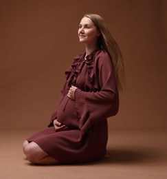 Photo of Beautiful pregnant woman in dress on brown background