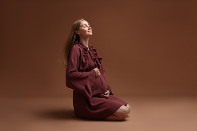 Photo of Beautiful pregnant woman in dress on brown background