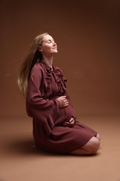 Photo of Beautiful pregnant woman in dress on brown background