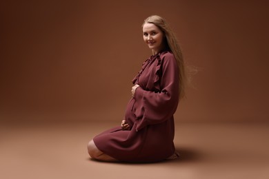Photo of Beautiful pregnant woman in dress on brown background