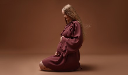 Photo of Beautiful pregnant woman in dress on brown background