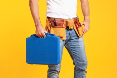 Photo of Professional repairman with tool box on orange background, closeup