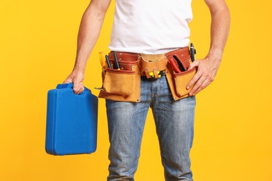 Photo of Professional repairman with tool box on orange background, closeup