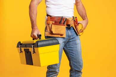 Photo of Professional repairman with tool box on orange background, closeup