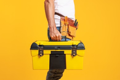 Photo of Professional repairman with tool box on orange background, closeup