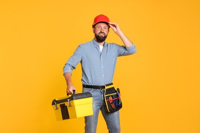 Photo of Professional repairman with tool box on orange background