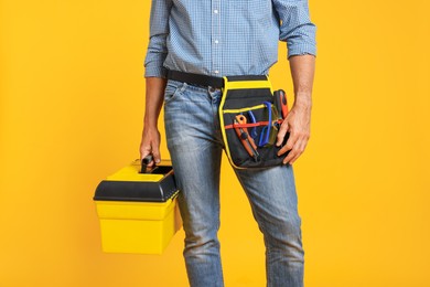 Photo of Professional repairman with tool box on orange background, closeup