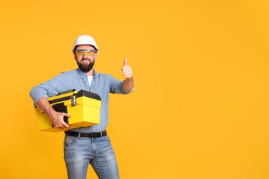 Photo of Professional repairman with tool box showing thumbs up on orange background, space for text