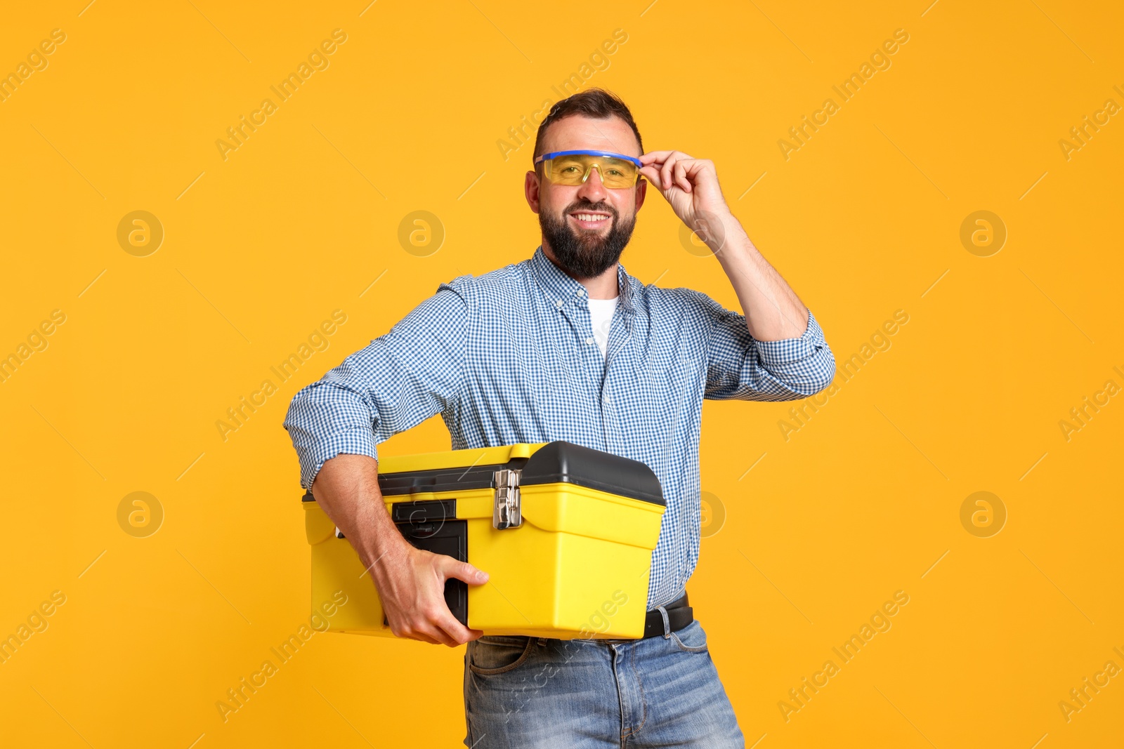 Professional repairman with tool box on orange background Photo of Professional repairman with tool box on orange background