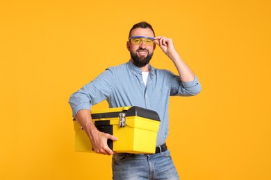 Photo of Professional repairman with tool box on orange background