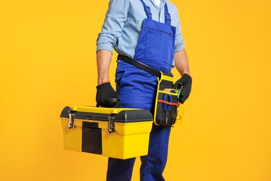 Photo of Professional repairman with tool box on orange background, closeup