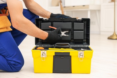 Photo of Professional repairman with tool box and pliers indoors, closeup