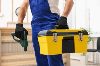Photo of Professional repairman with tool box and electric screwdriver indoors, closeup