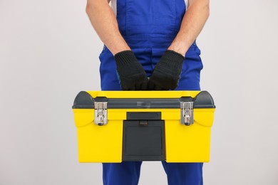 Photo of Professional repairman with tool box on light grey background, closeup