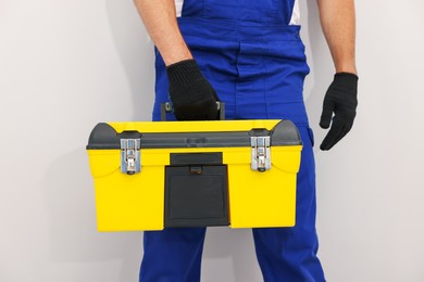 Photo of Professional repairman with tool box on light grey background, closeup